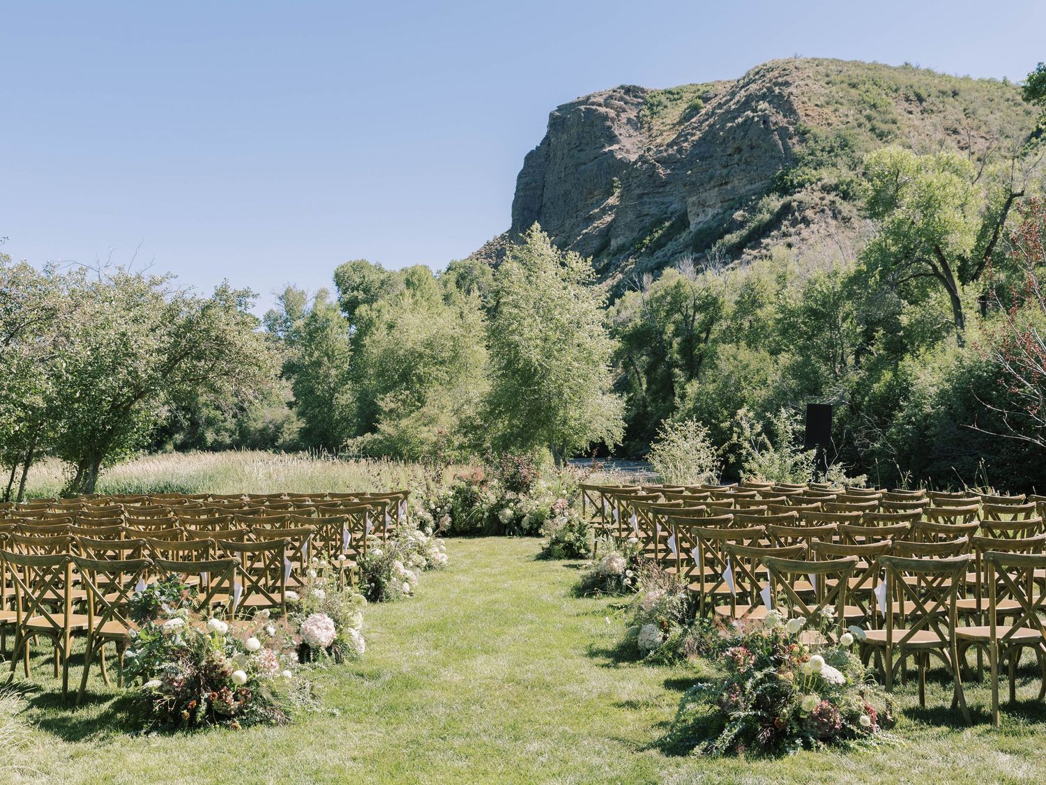Wooden chairs arranged in rows for an outdoor wedding ceremony with a dramatic mountain cliff backdrop in nature.
