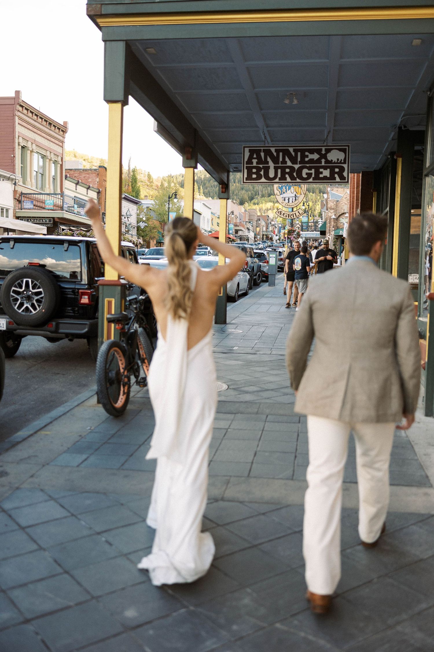 Wedding couple walking and dancing along a sidewalk under storefront awnings.