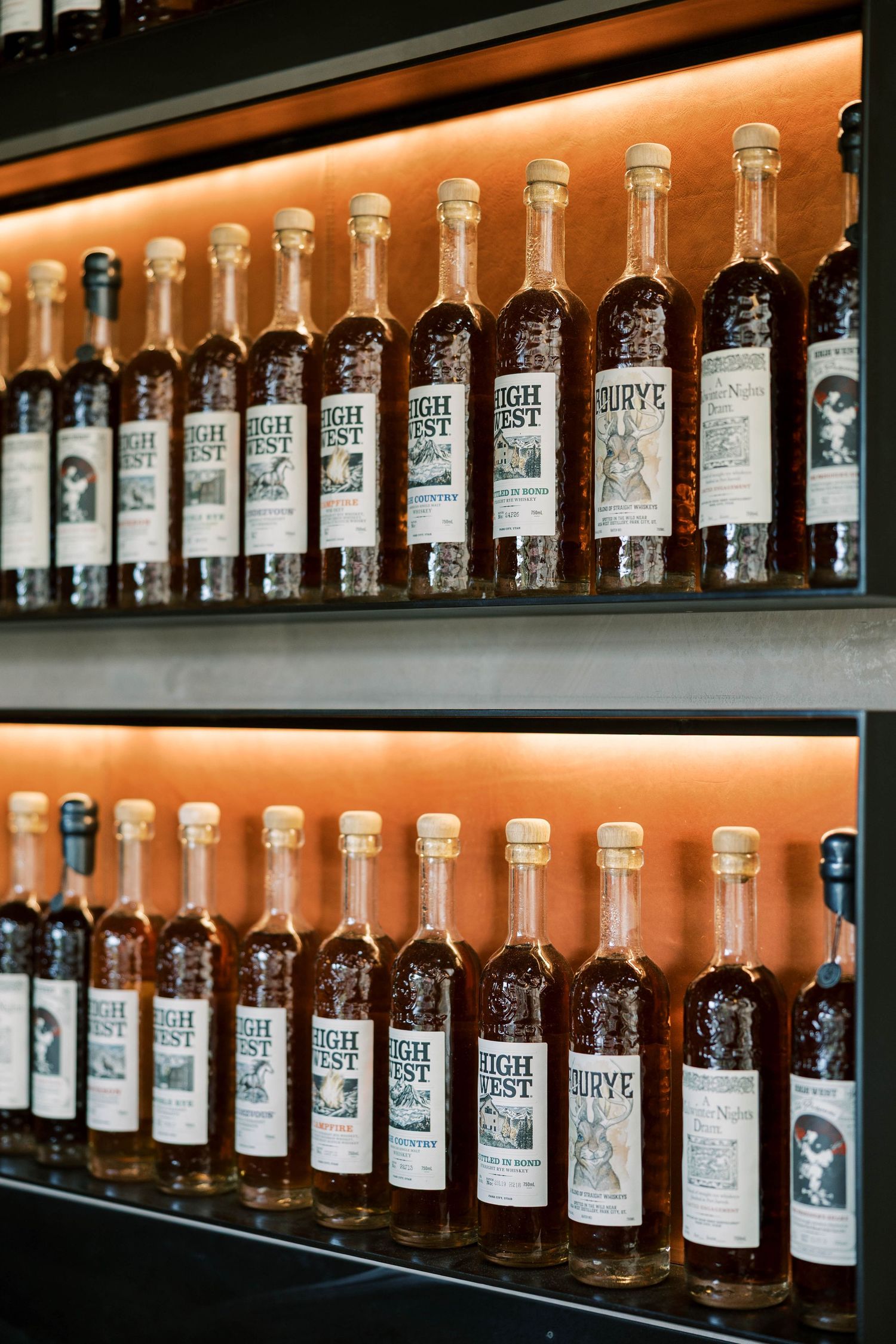 Long shelf display of illuminated whiskey bottles in a distillery tasting room.