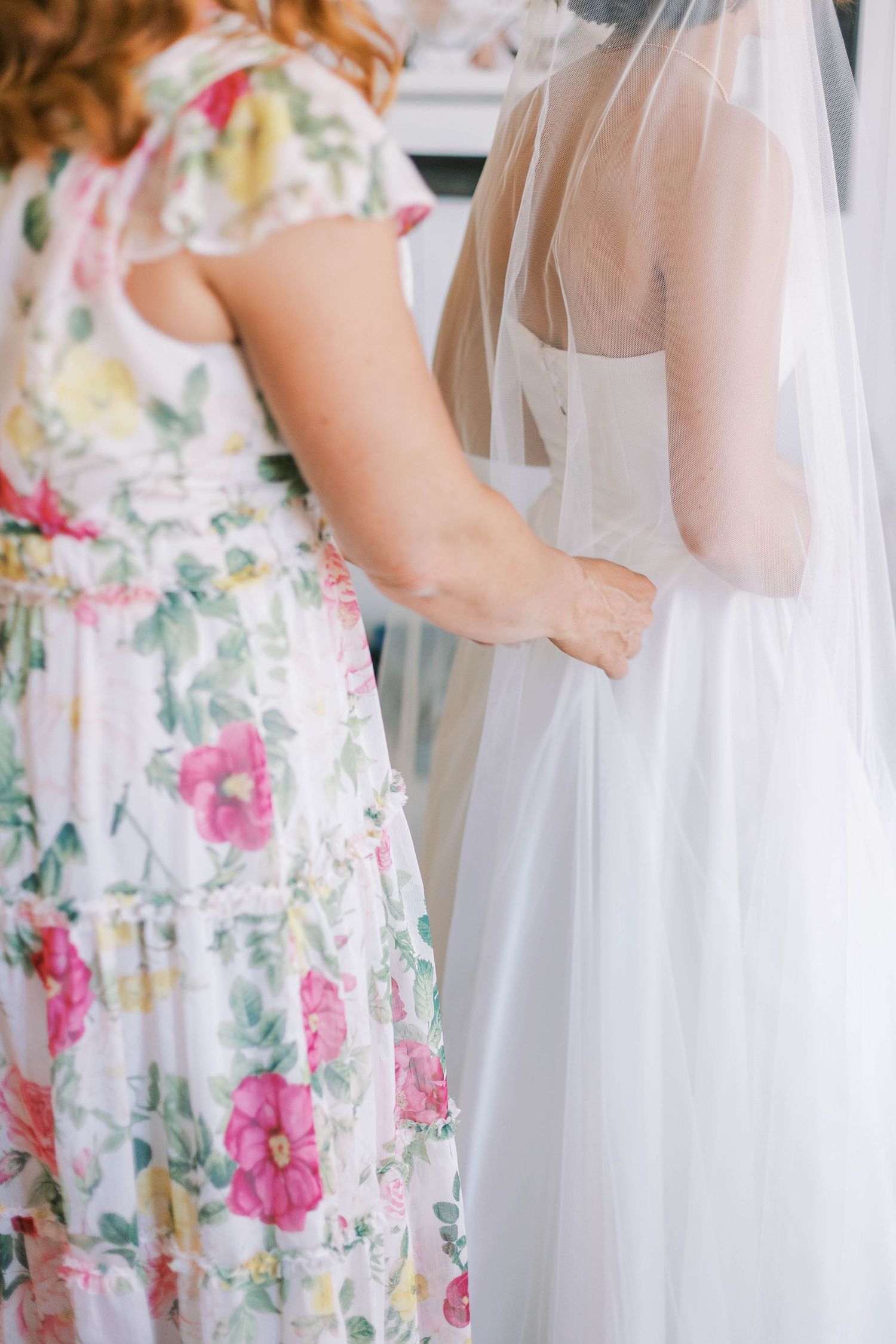 A floral bridesmaid dress is shown next to a white wedding gown in a bridal preparation scene.