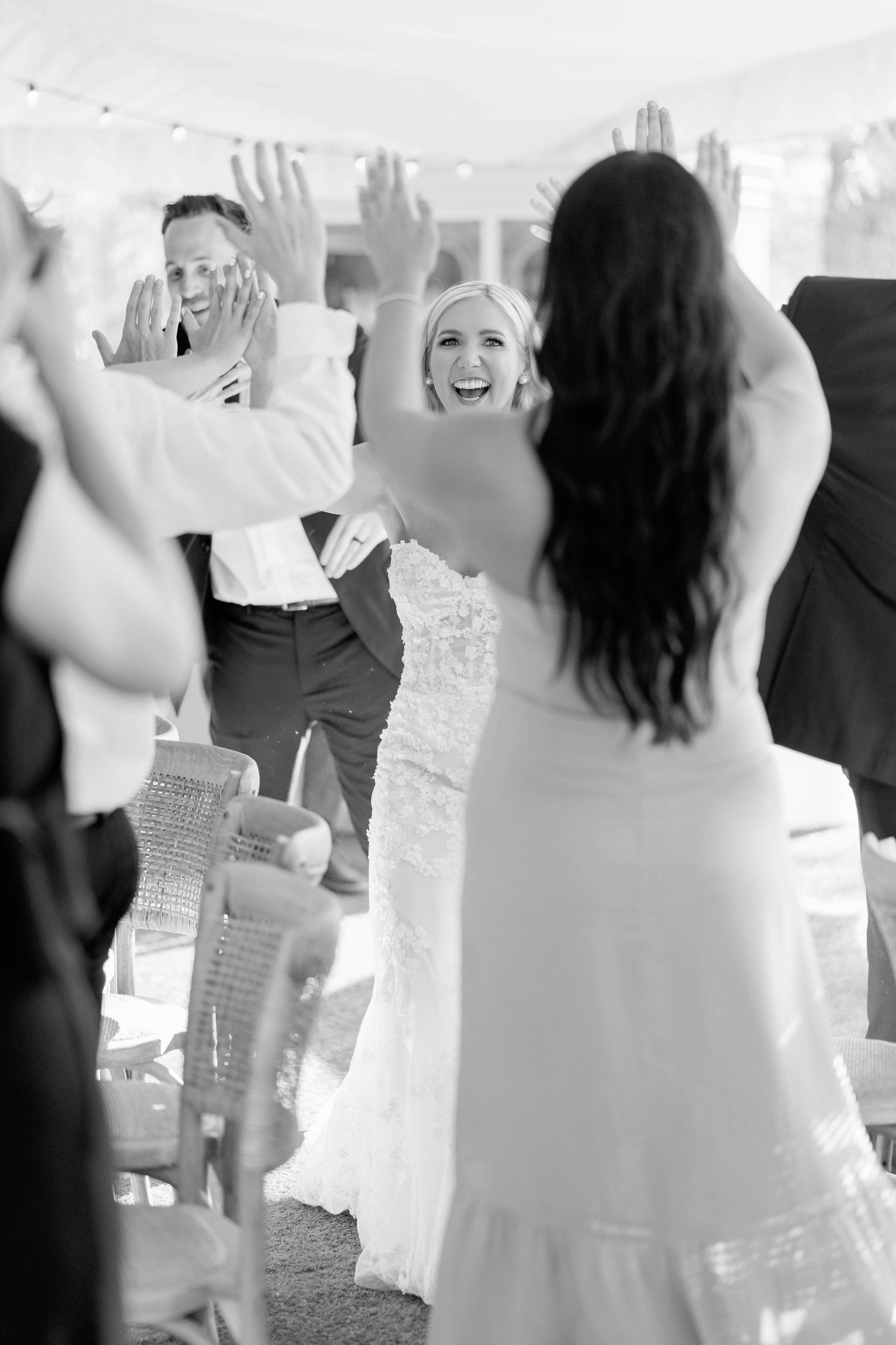 Wedding celebration with guests dancing and raising their hands joyfully under a tent.