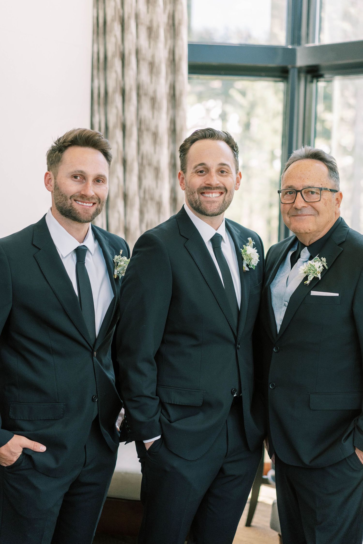 Three men in dark suits pose together wearing matching boutonnieres.