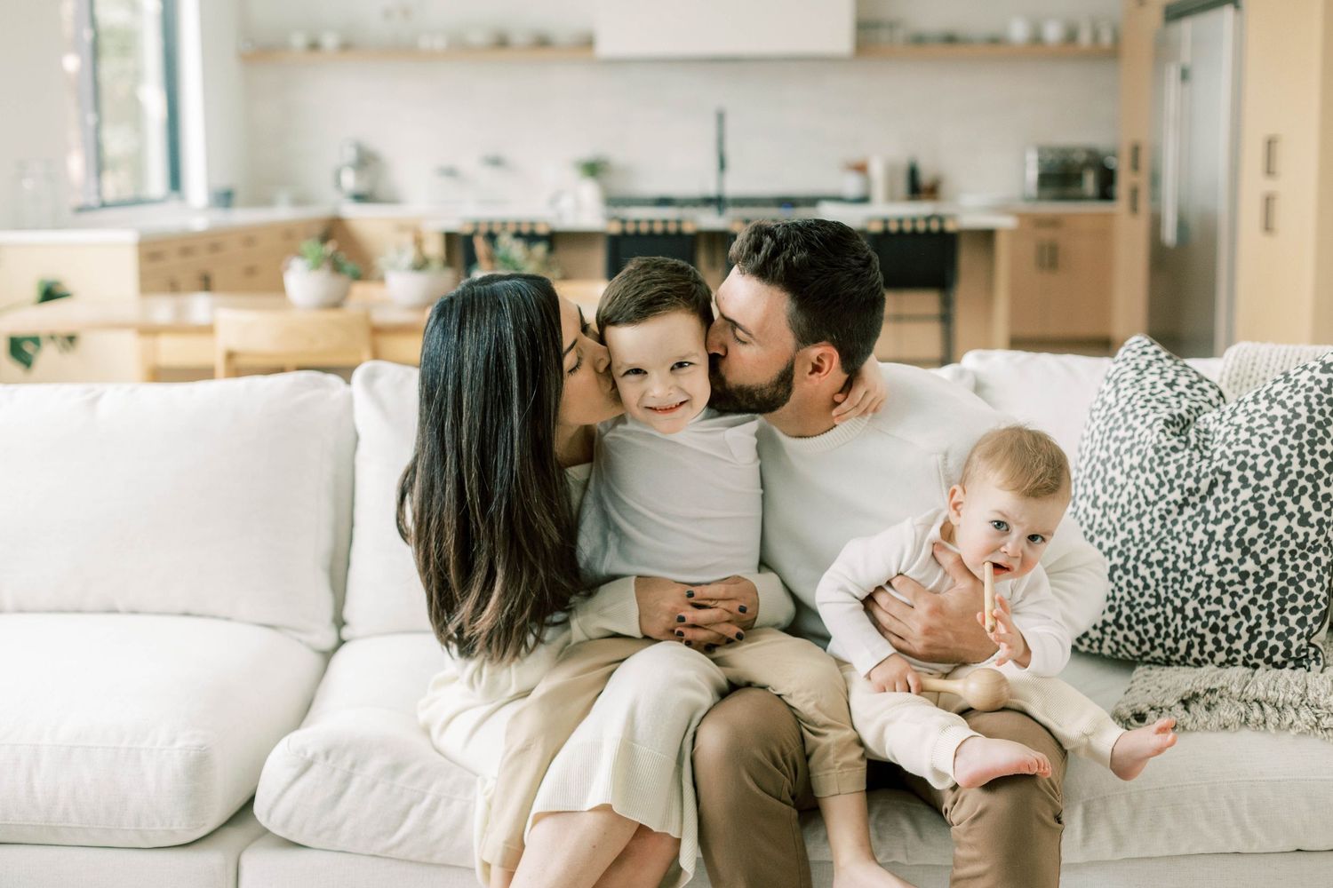 Family sharing tender moment together on white couch in modern minimalist living room with kitchen.