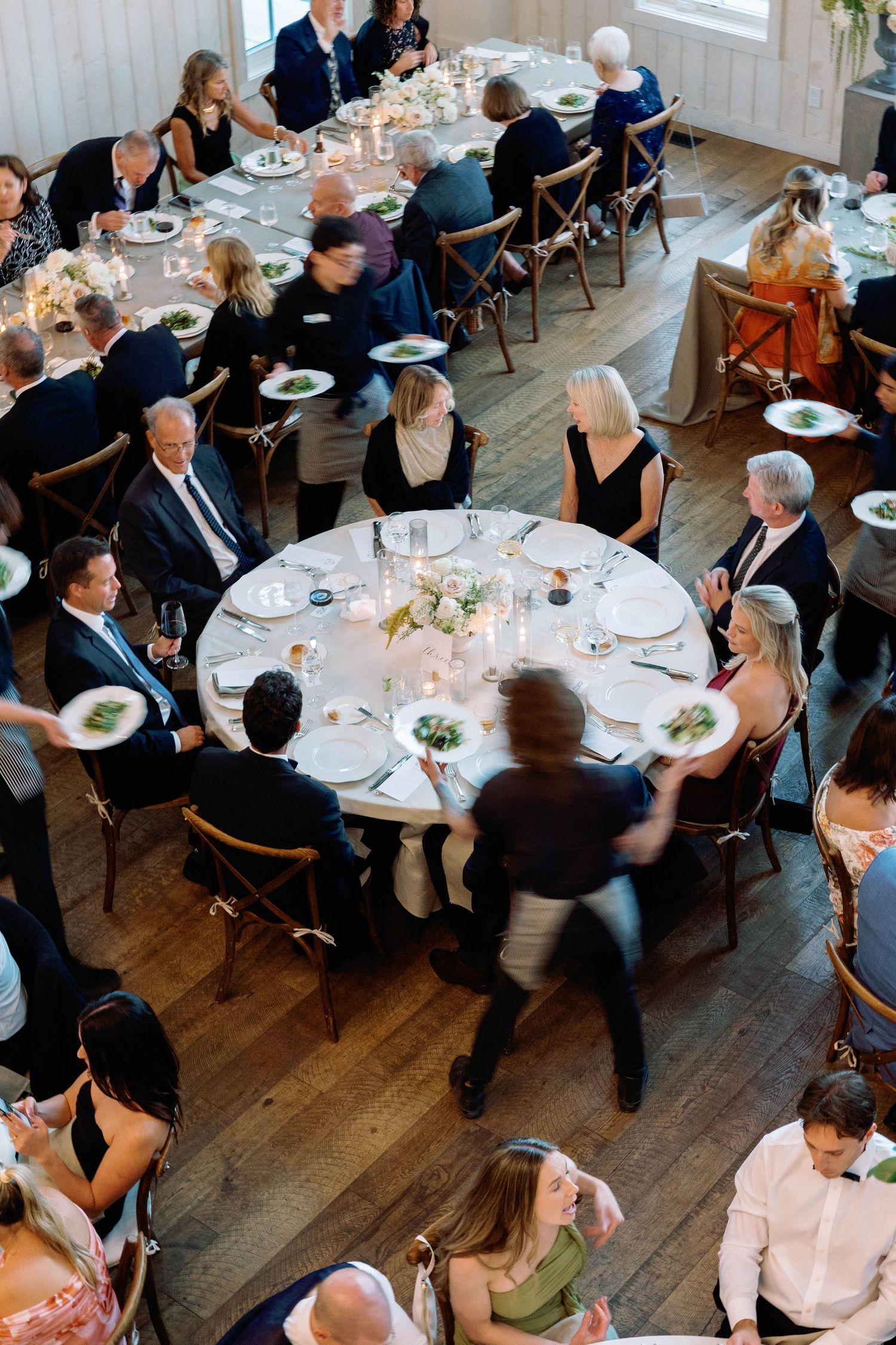Overhead view of elegant wedding reception with guests seated at round tables in a rustic venue with hardwood floors.