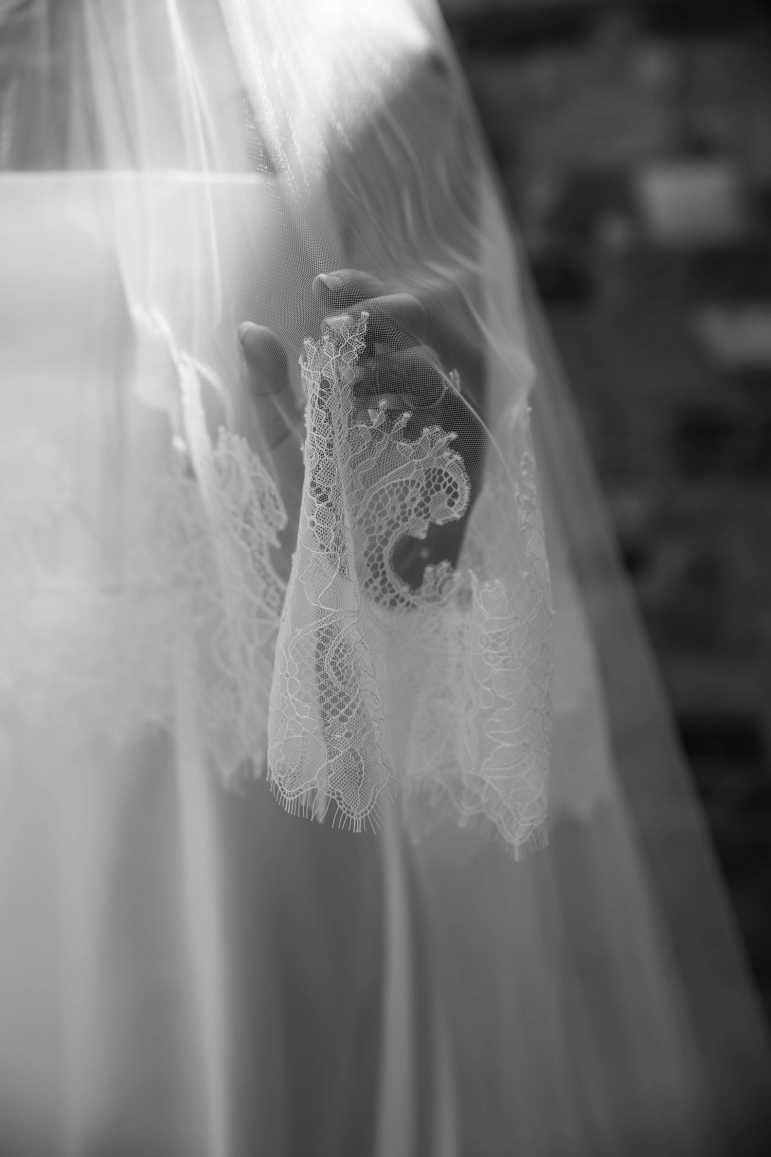A delicate lace wedding veil detail shown in soft black and white with intricate floral patterns visible through the sheer fabric.