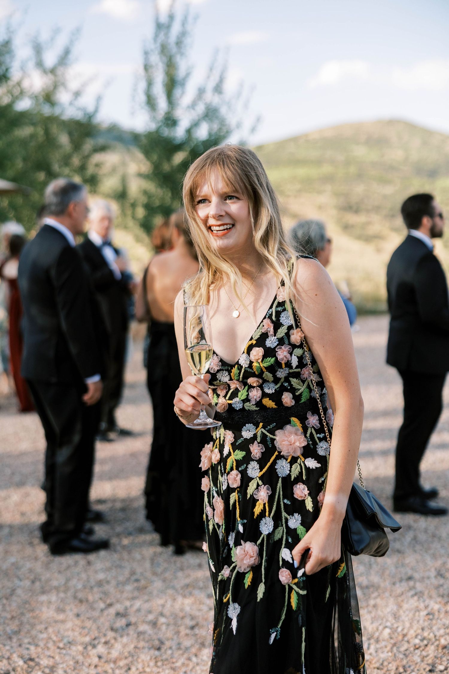 Wedding guests mingling outdoors at a reception with person in floral dress.