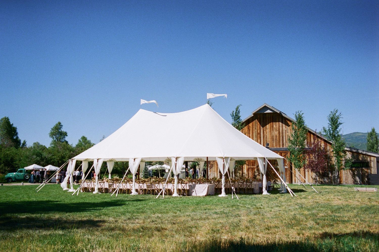 Large white wedding tent setup in a scenic outdoor venue with rustic barn and rolling hills in the background.