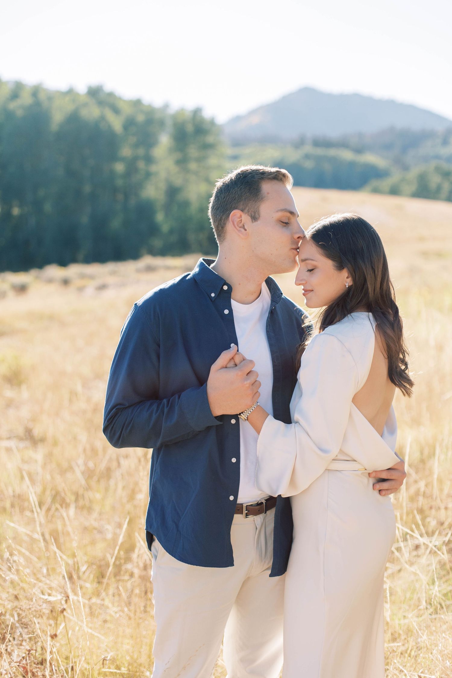 A romantic embrace in a sunny mountain meadow with couple wearing coordinated white and navy outfits.