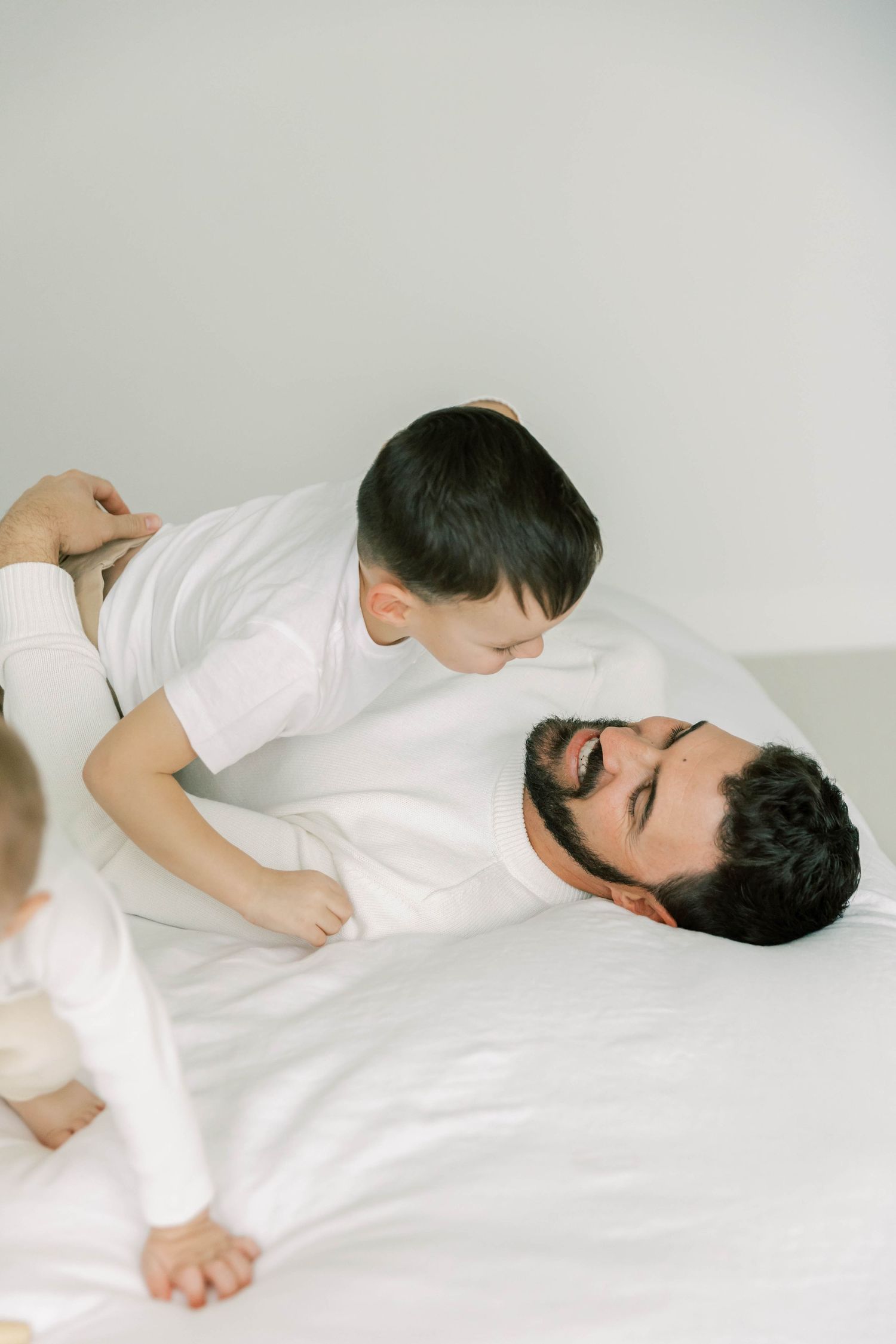 Father and child playing together while lying on white bed.