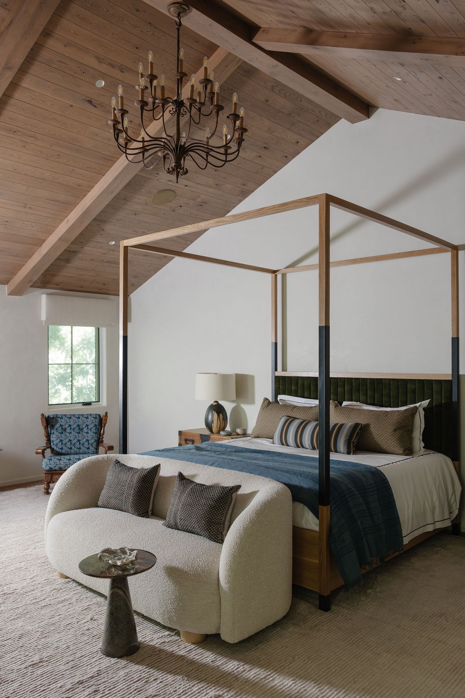 Elegant four-poster bed in vaulted wood ceiling bedroom with chandelier, cream sofa, and blue accents.