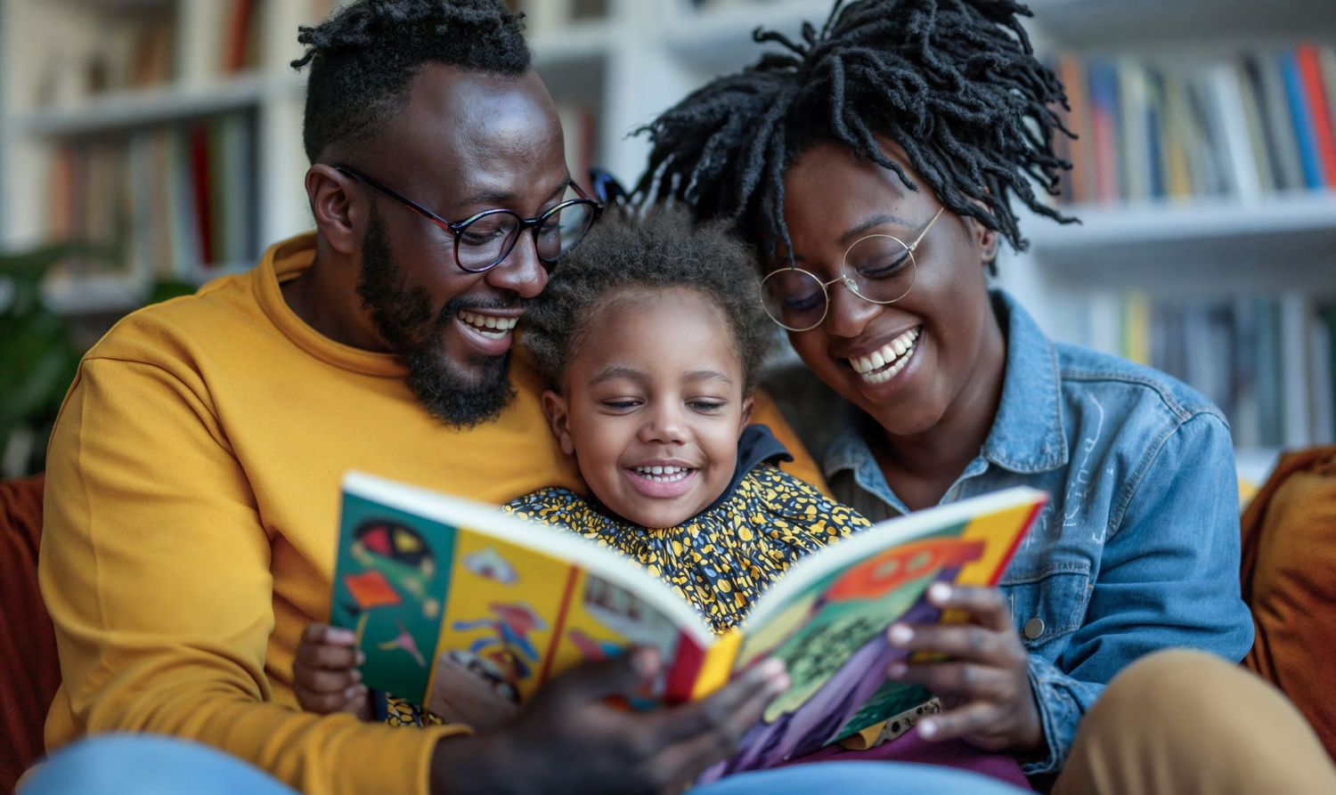 Happy Black family with two parents and child reading colorful picture book together.