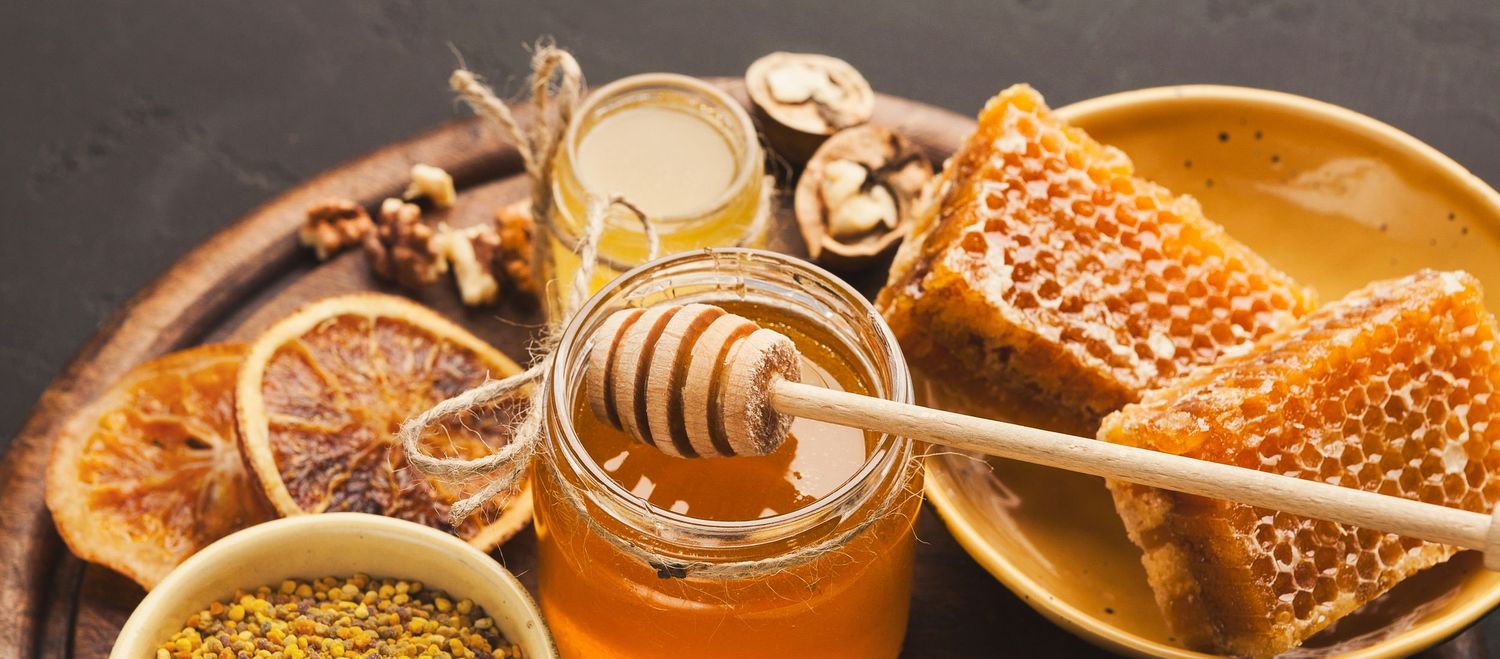 Assorted honey products including honeycomb, honey dipper, bee pollen, and dried orange slices.