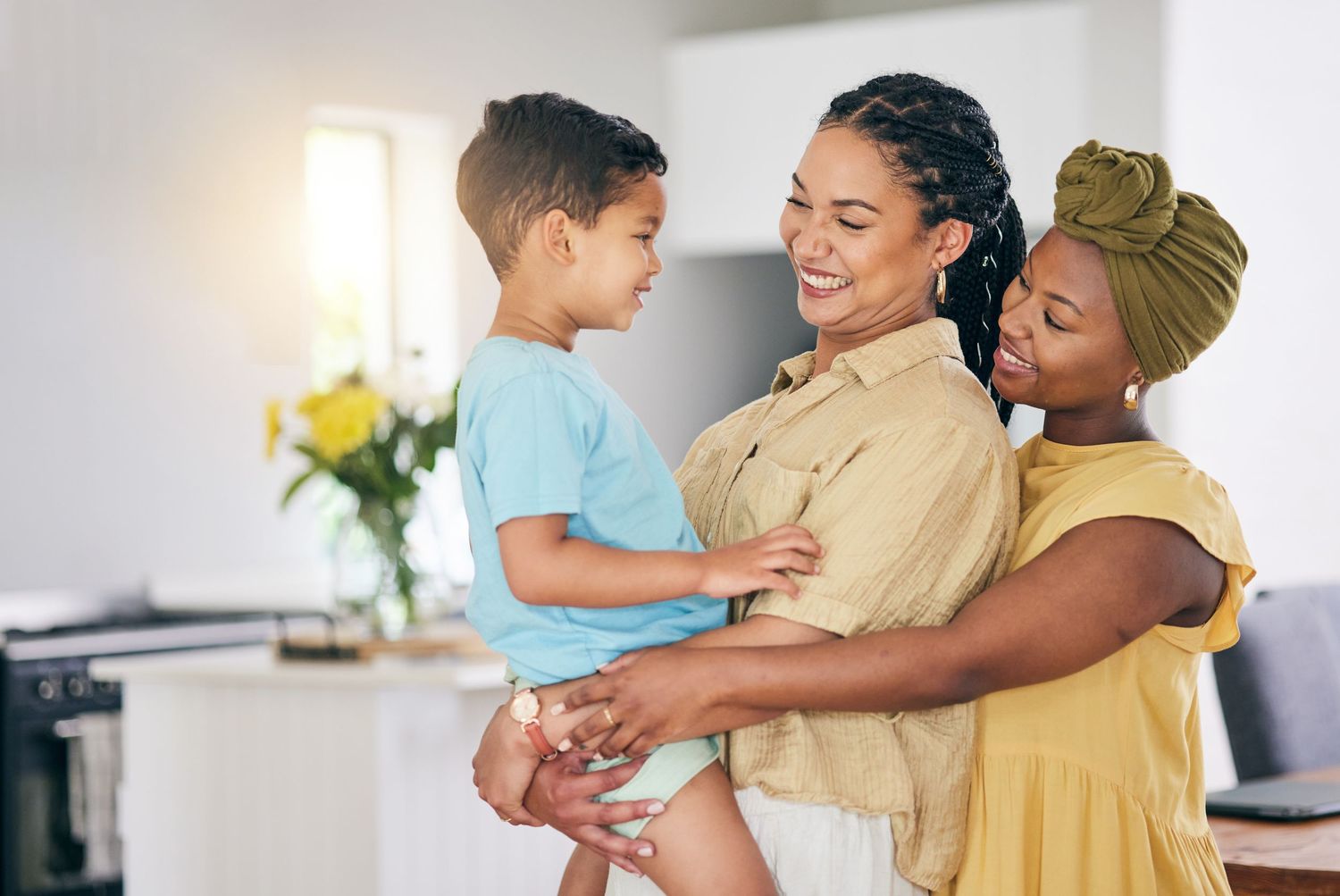 Two women smiling and bonding with a happy young boy in a bright modern home interior.