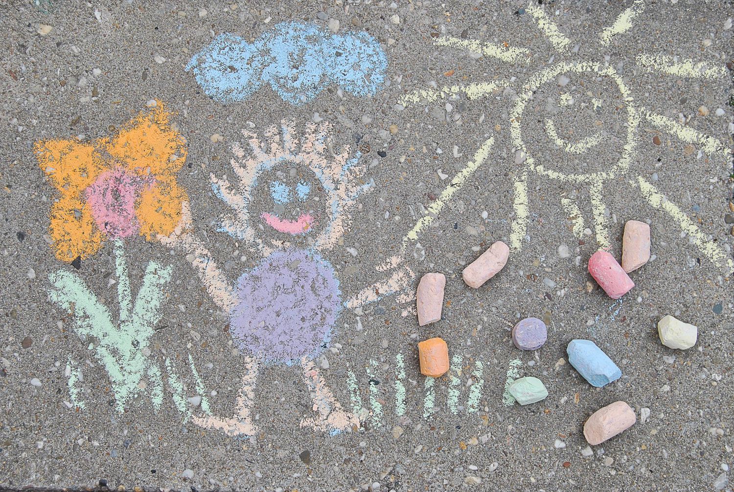 Colorful chalk drawing of a person, flowers, and sun on a sidewalk with chalk pieces nearby.