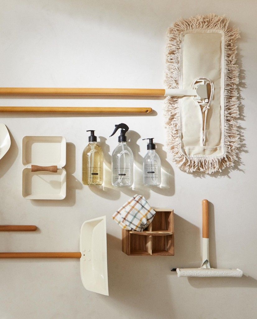 Minimalist wall display of cleaning supplies, spray bottles, mop, and wooden organizers on white wall.