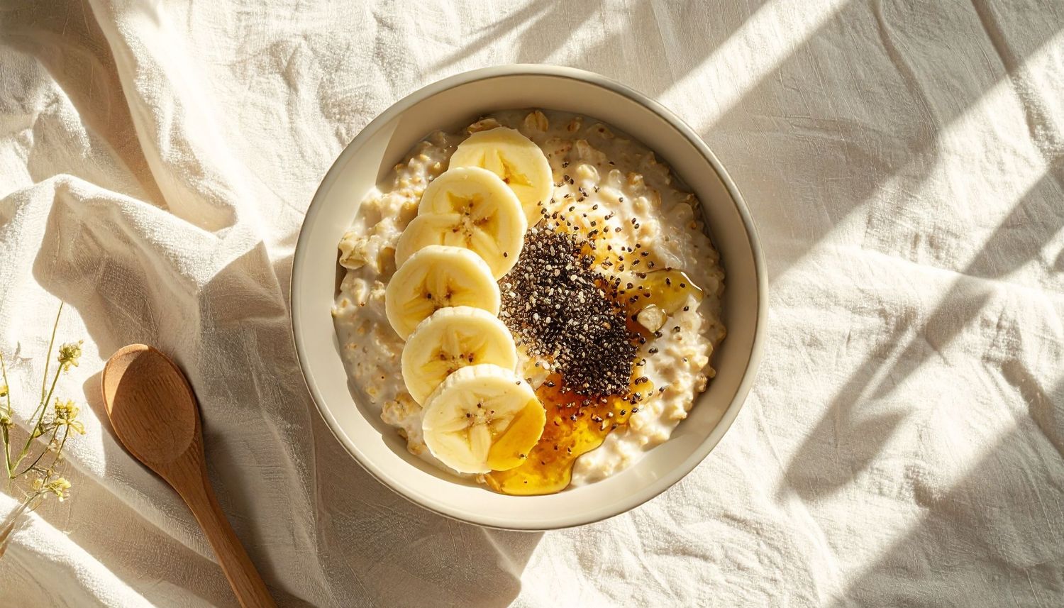 Overhead view of creamy oatmeal topped with banana slices, chia seeds, and honey in a white bowl.
