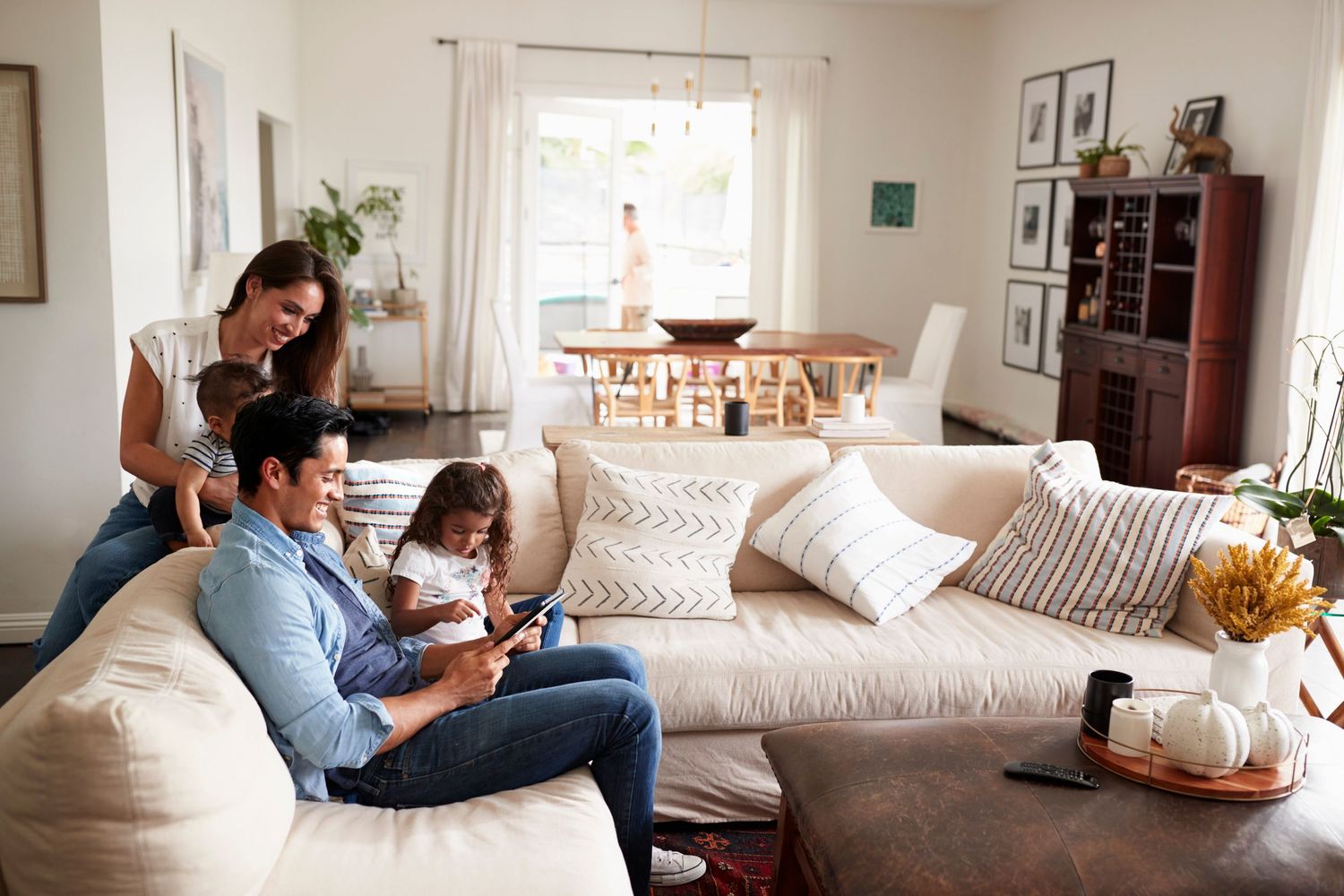 Family of three relaxing on a white sofa in a bright living room, parents and child sharing a smartphone together.