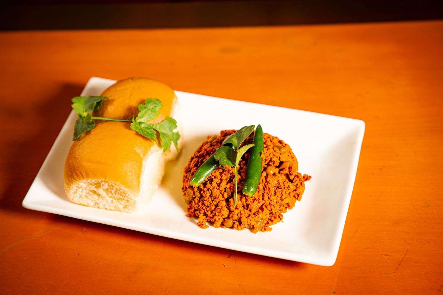 White plate with orange rice dish garnished with basil leaves and orange citrus segments on a wooden table.