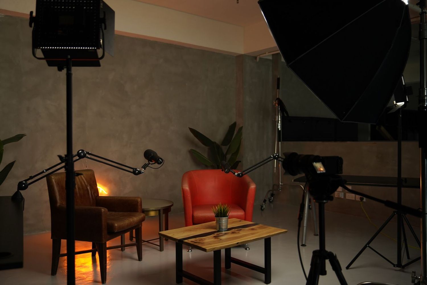 Photography studio setup with lighting equipment, reflectors, wooden chair and table against grey wall interior.