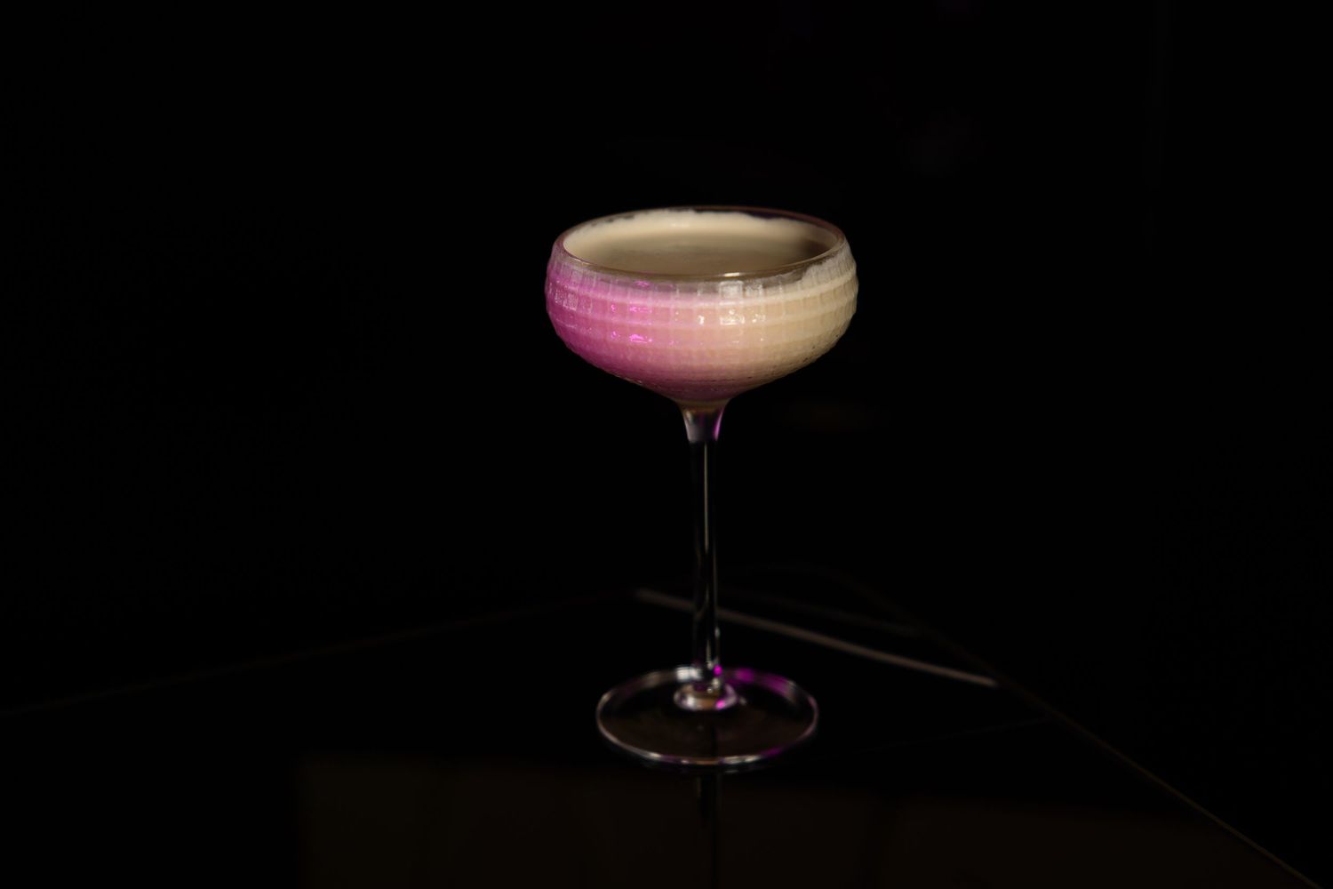 An elegant pink cocktail served in a coupe glass against a dark background.
