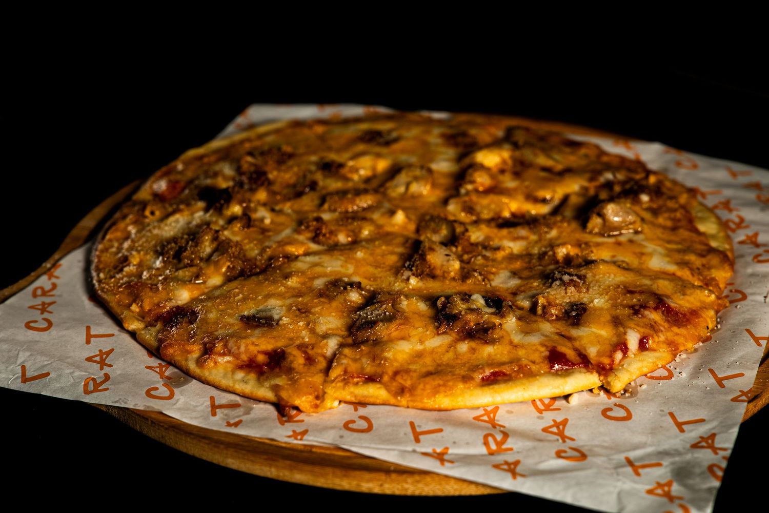 Freshly baked pizza with melted cheese and toppings on branded paper against dark background.