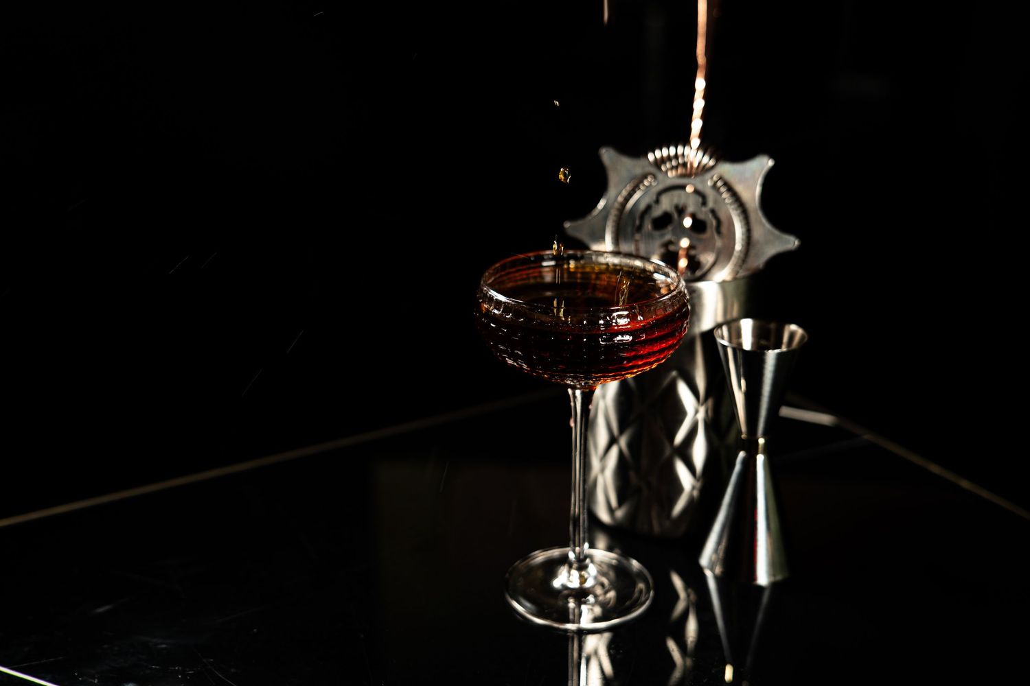 A glass of red wine sits elegantly on a dark reflective surface with a metallic wine opener in the background.