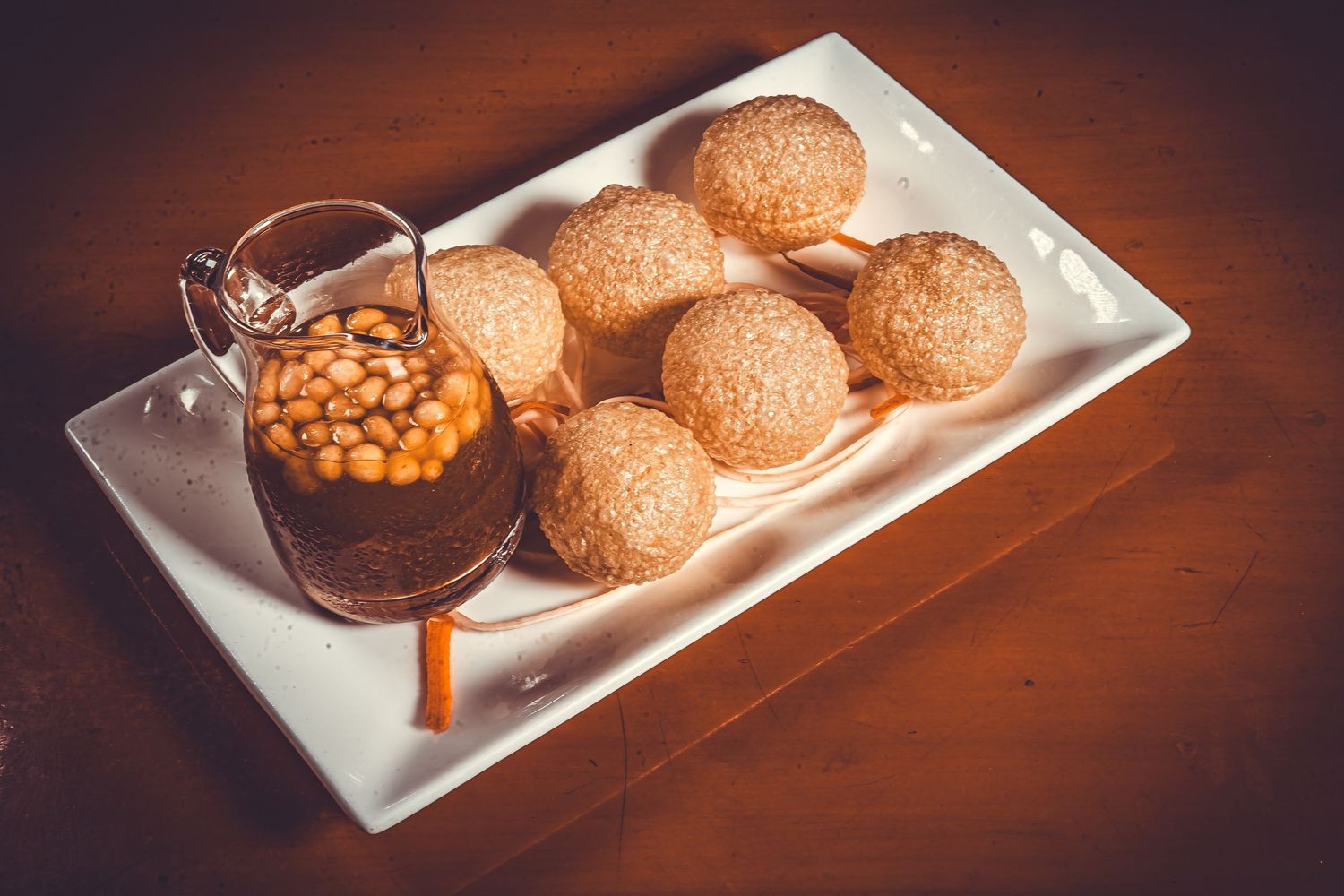 Six sesame seed hamburger buns on a white plate with a side of golden baked beans in dark lighting.