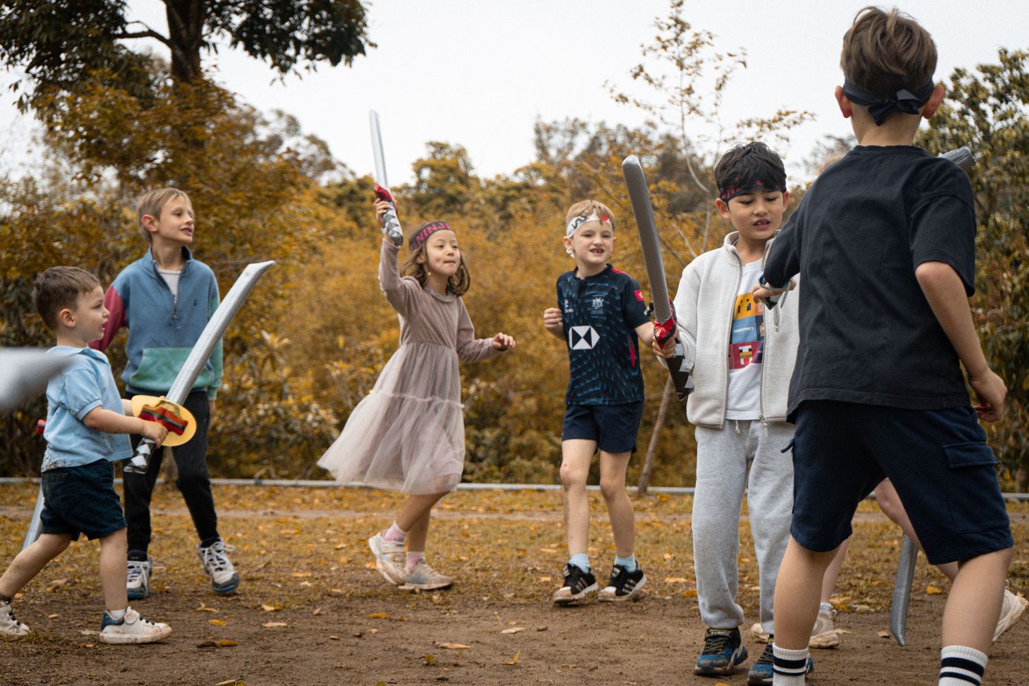 Group of children playing with toy swords in an outdoor autumn setting.