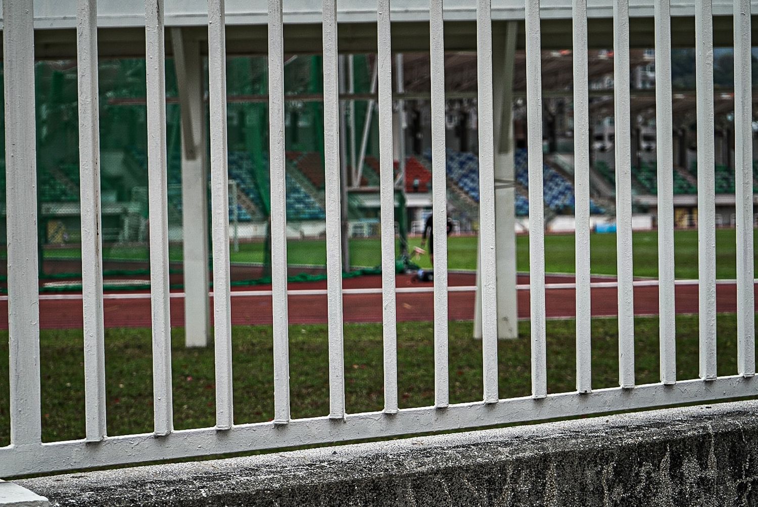 White metal railing bars in front of a sports field or stadium track.