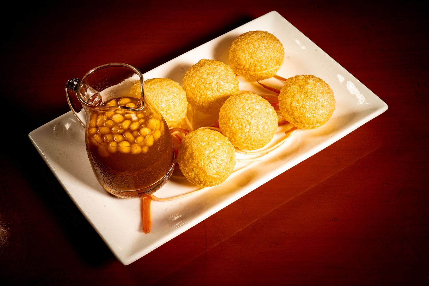 Round golden fried dumplings served with a side of beans in dark sauce on white rectangular plate.