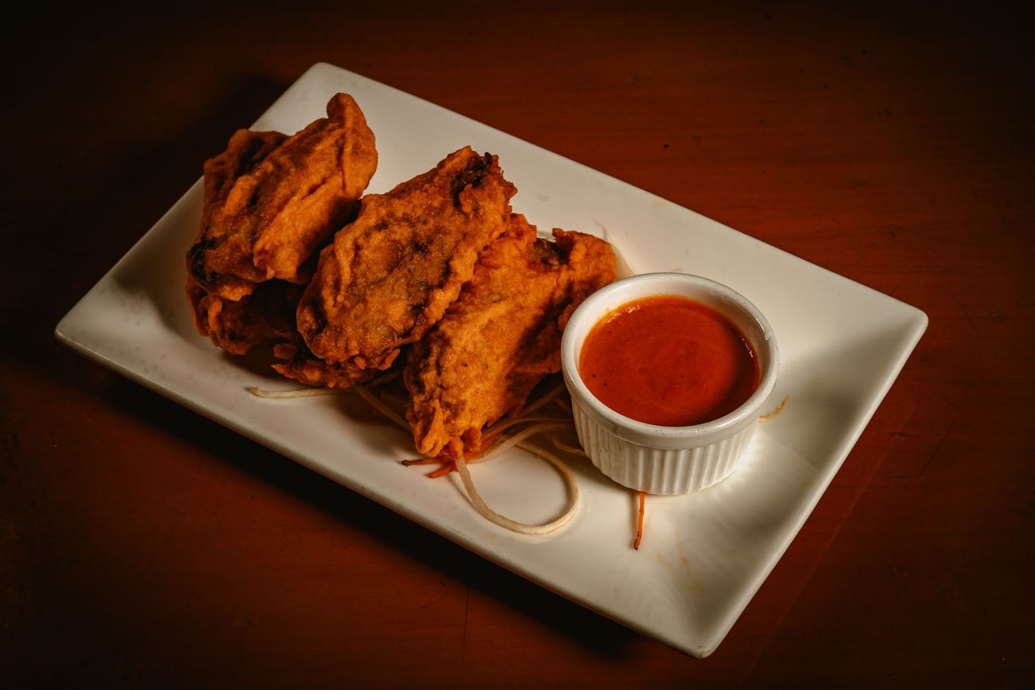 Crispy tandoori chicken pieces served with spicy red dipping sauce on white rectangular plate.