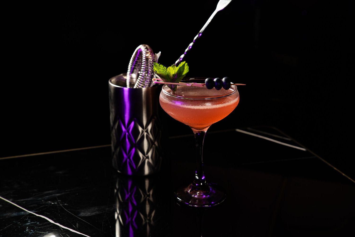 Two craft cocktails displayed with one in a decorative purple vessel and another in a coupe glass.