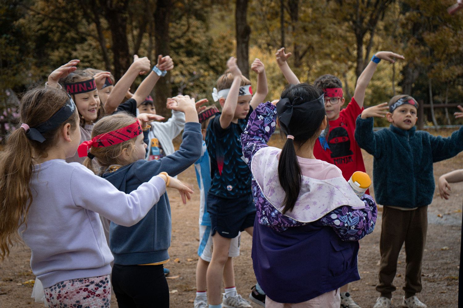 Energetic group performs synchronized dance moves with raised arms in autumn outdoor setting.