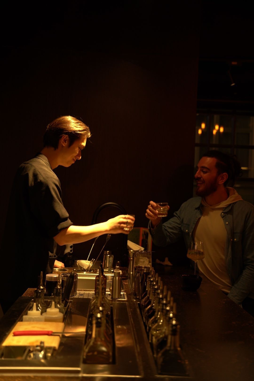 A bartender serves drinks to a customer at a dimly lit bar counter.