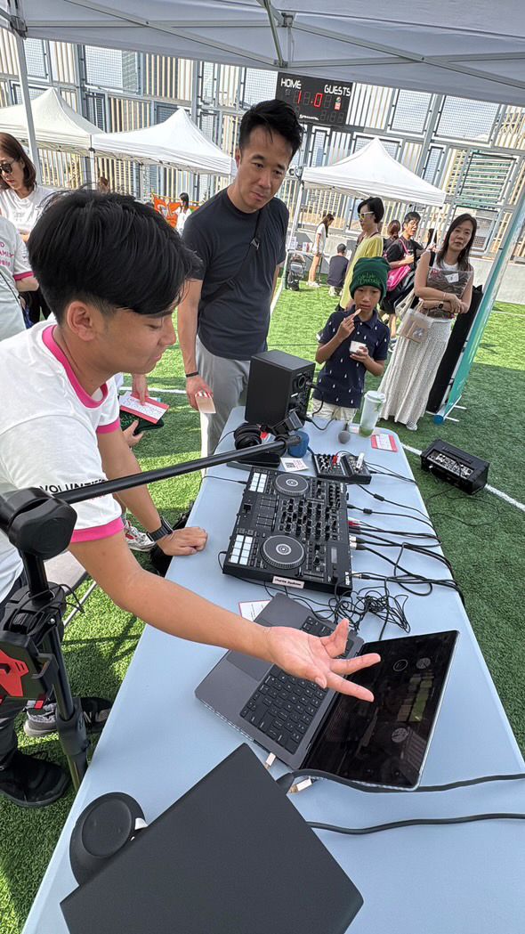 DJ equipment and mixer setup on a table at an outdoor event with people gathered around on artificial turf.