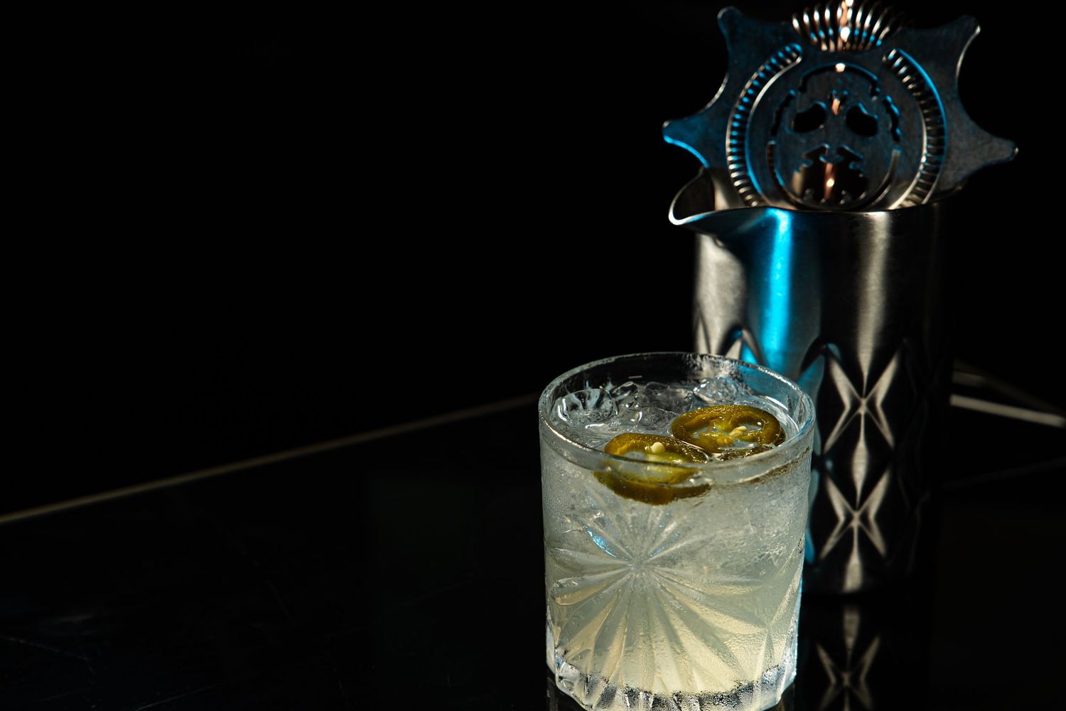 An elegant cocktail glass with citrus garnish sits beside a sleek metallic cocktail shaker on a dark surface.