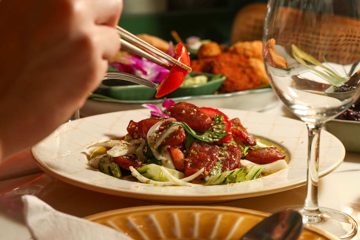 A colorful salad with fresh vegetables and red dressing being enjoyed at a formal dining table with wine glasses.