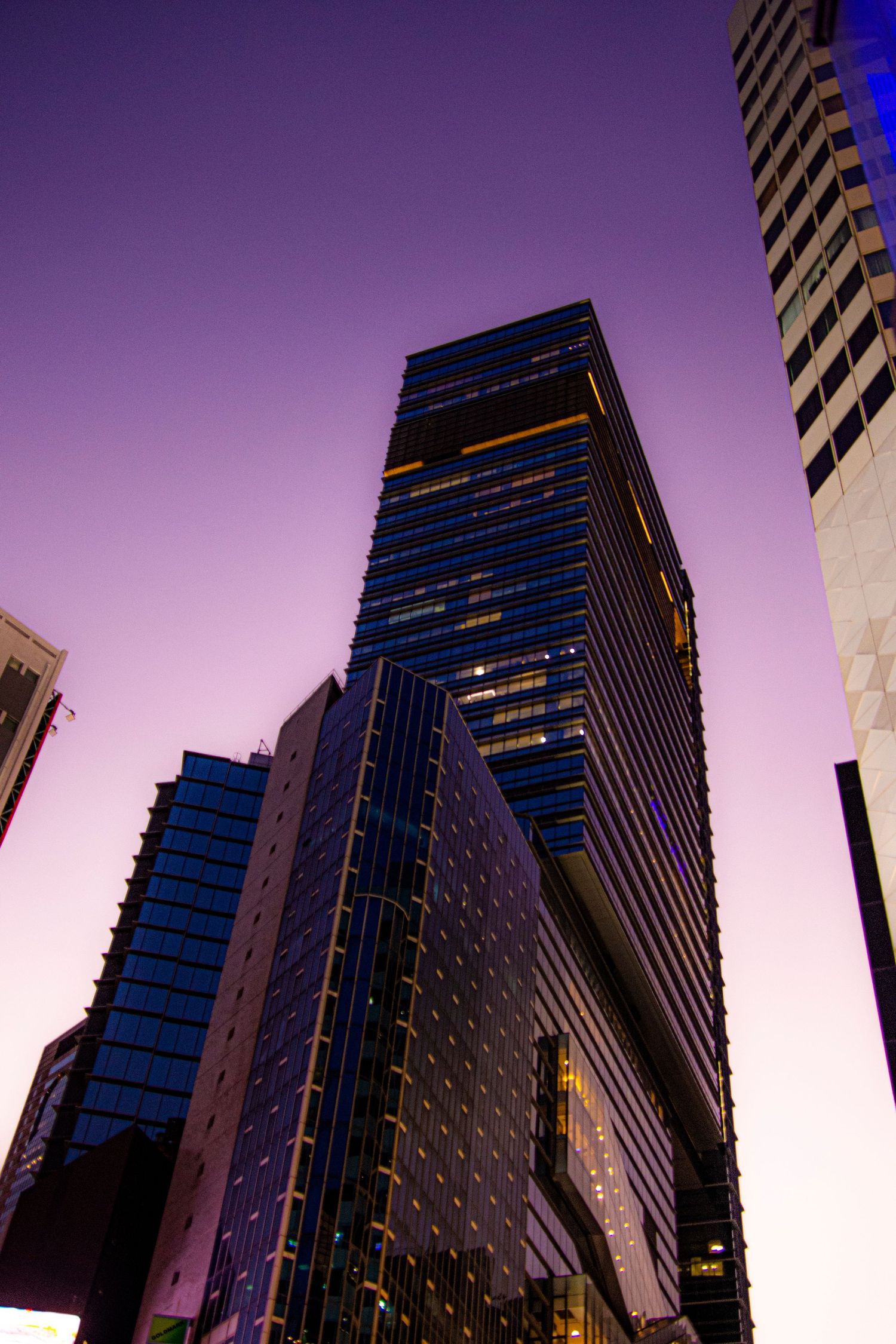 Modern glass skyscraper illuminated against purple twilight sky in urban setting.