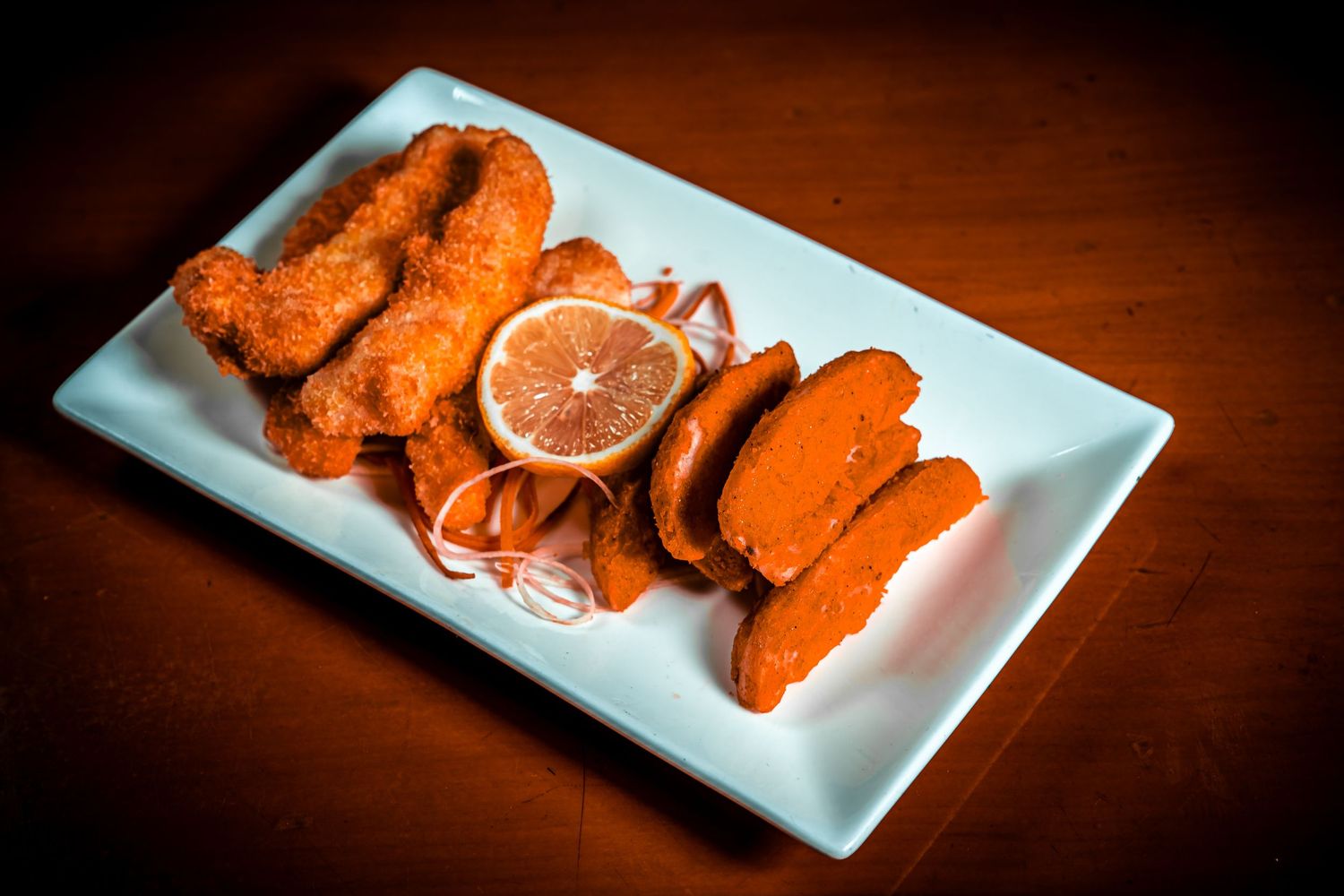 Orange-colored buffalo wings arranged with lemon slice on white rectangular plate.