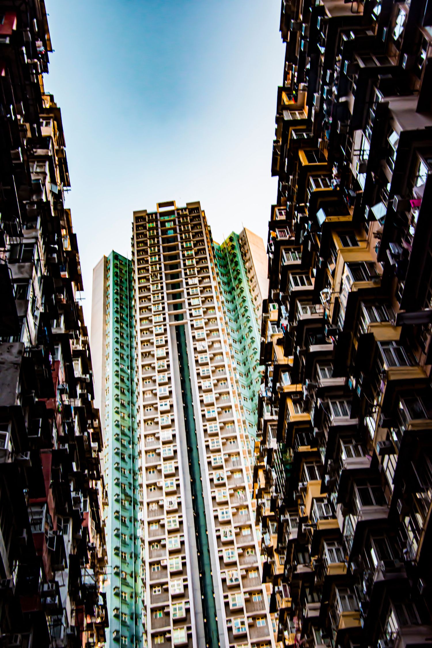 Dense residential apartment buildings shot from below against blue sky in Hong Kong.