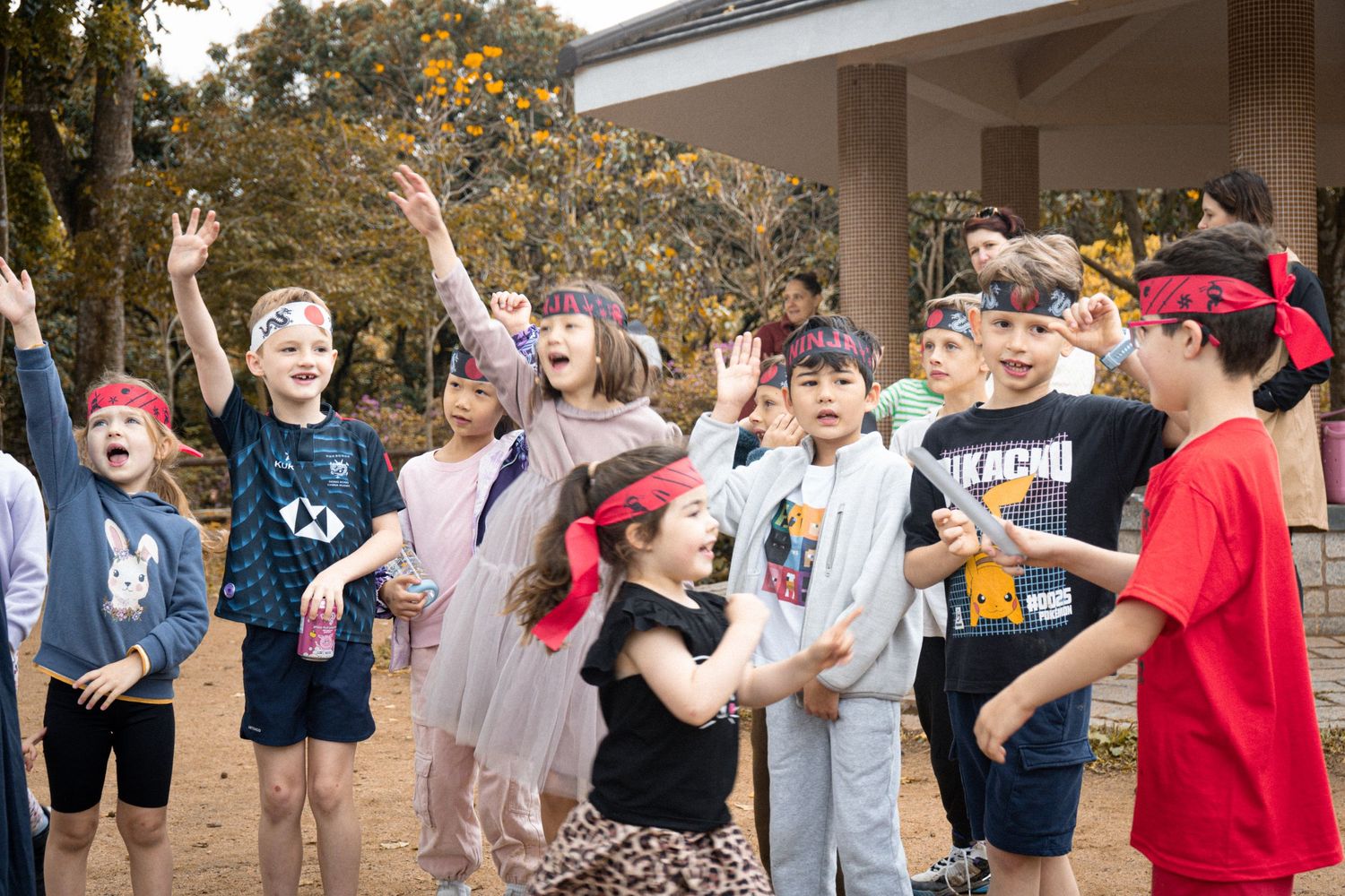 Group of excited children with hands raised in joyful celebration during outdoor event in scenic mountain setting.