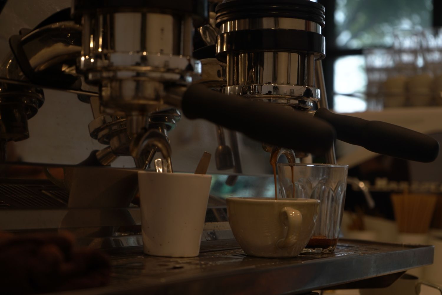Coffee machine brewing espresso into white cups in dark ambient setting.