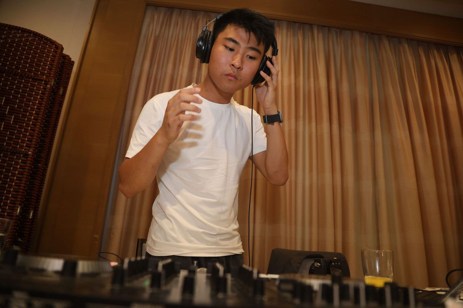 DJ wearing headphones while mixing and performing at turntables in a warmly lit room.