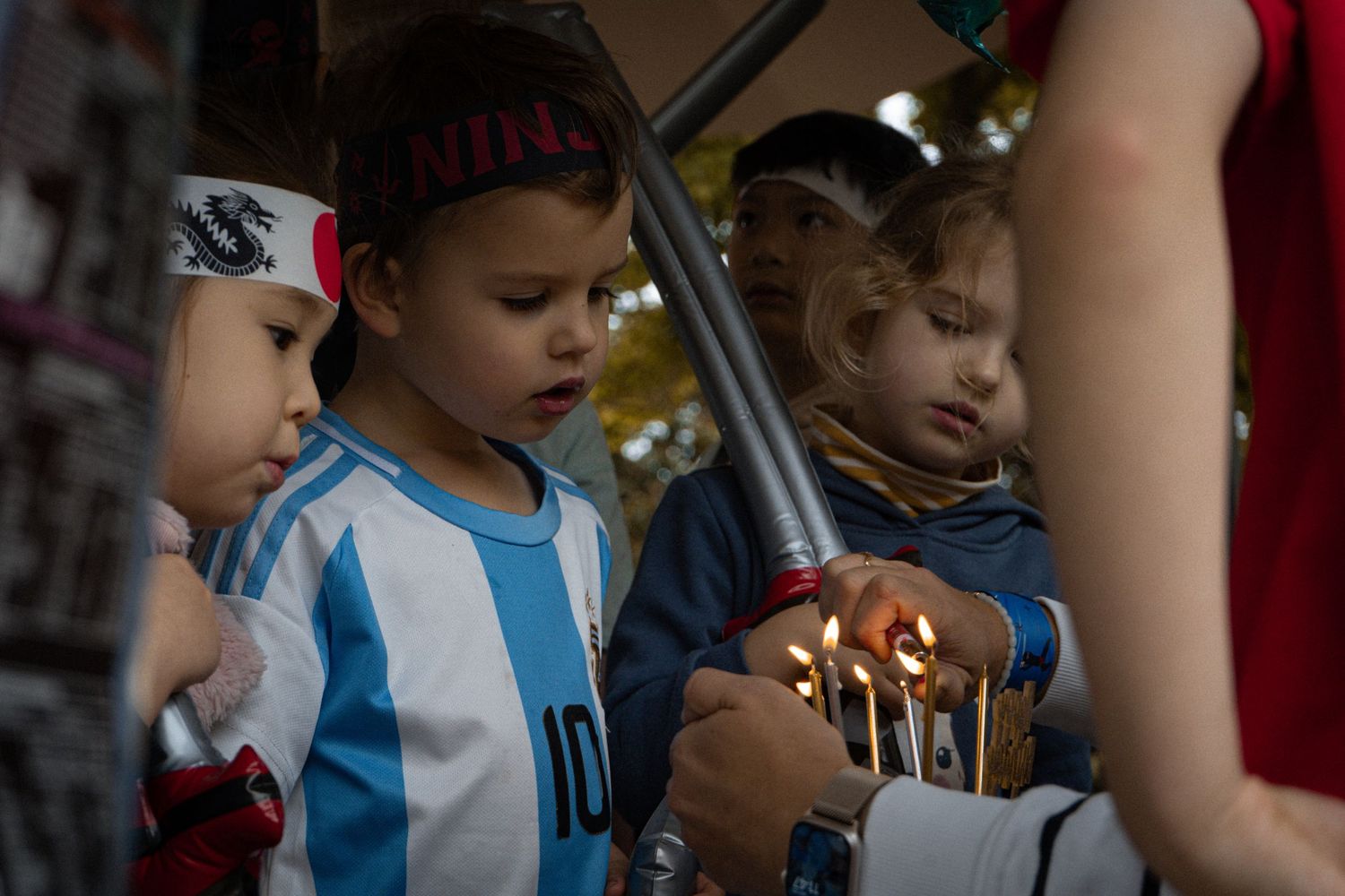 Young children gathered around candles in celebration wearing party attire.