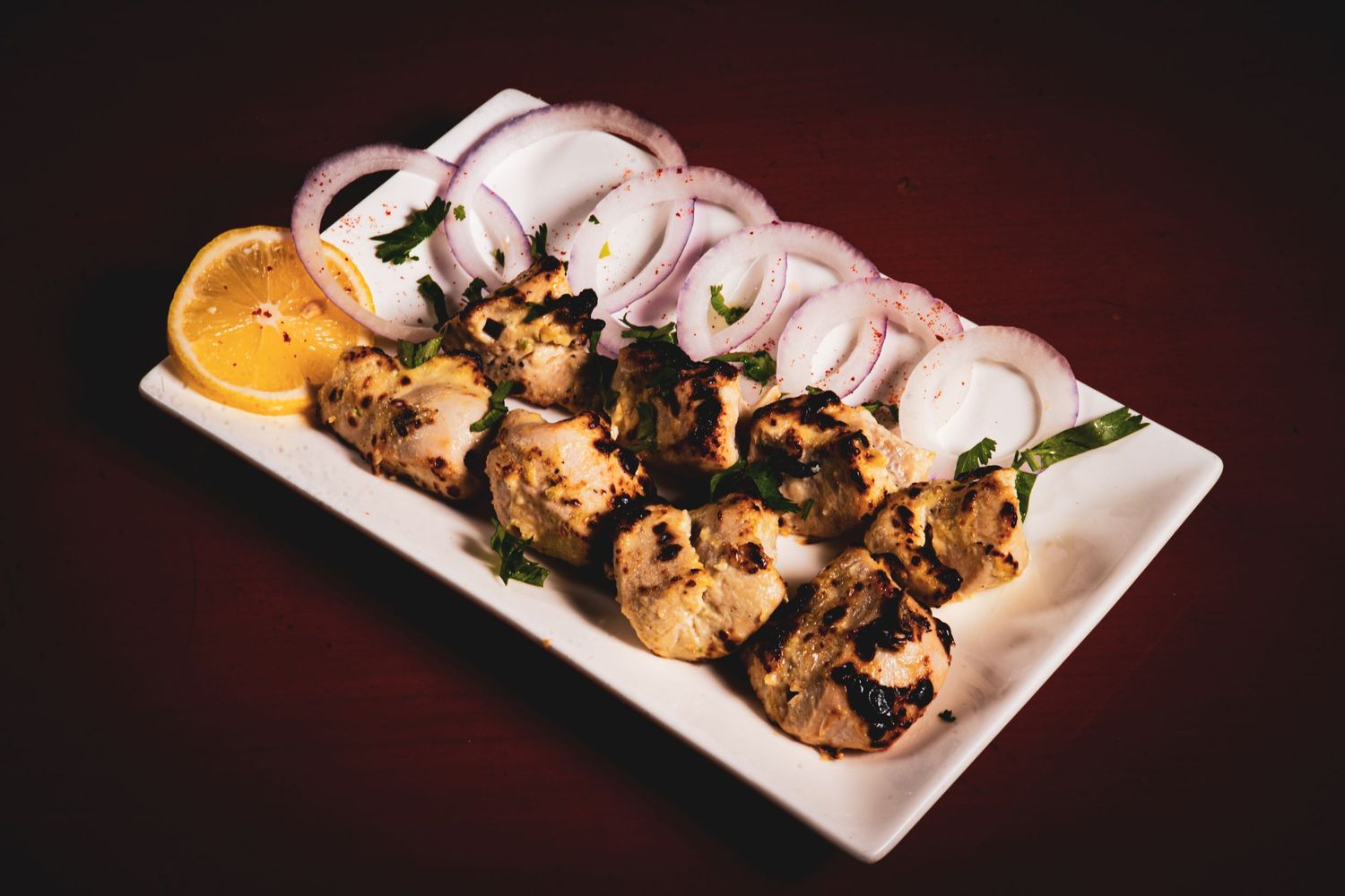 Grilled meat skewers garnished with sliced onions served on a white rectangular plate.