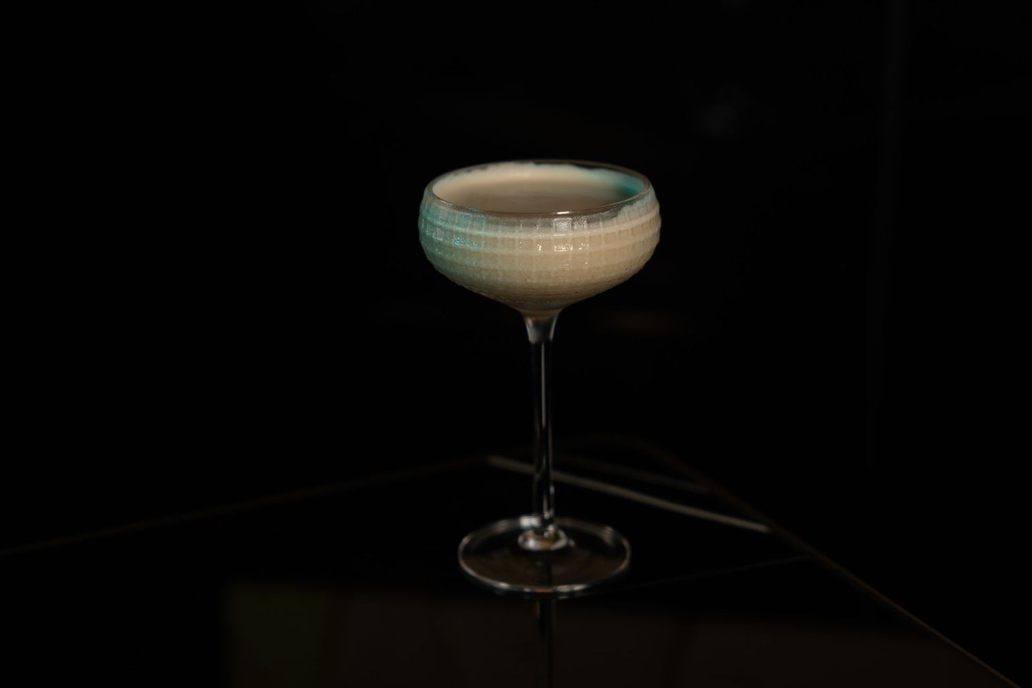 A sophisticated blue-tinted cocktail served in a coupe glass against a dark backdrop.
