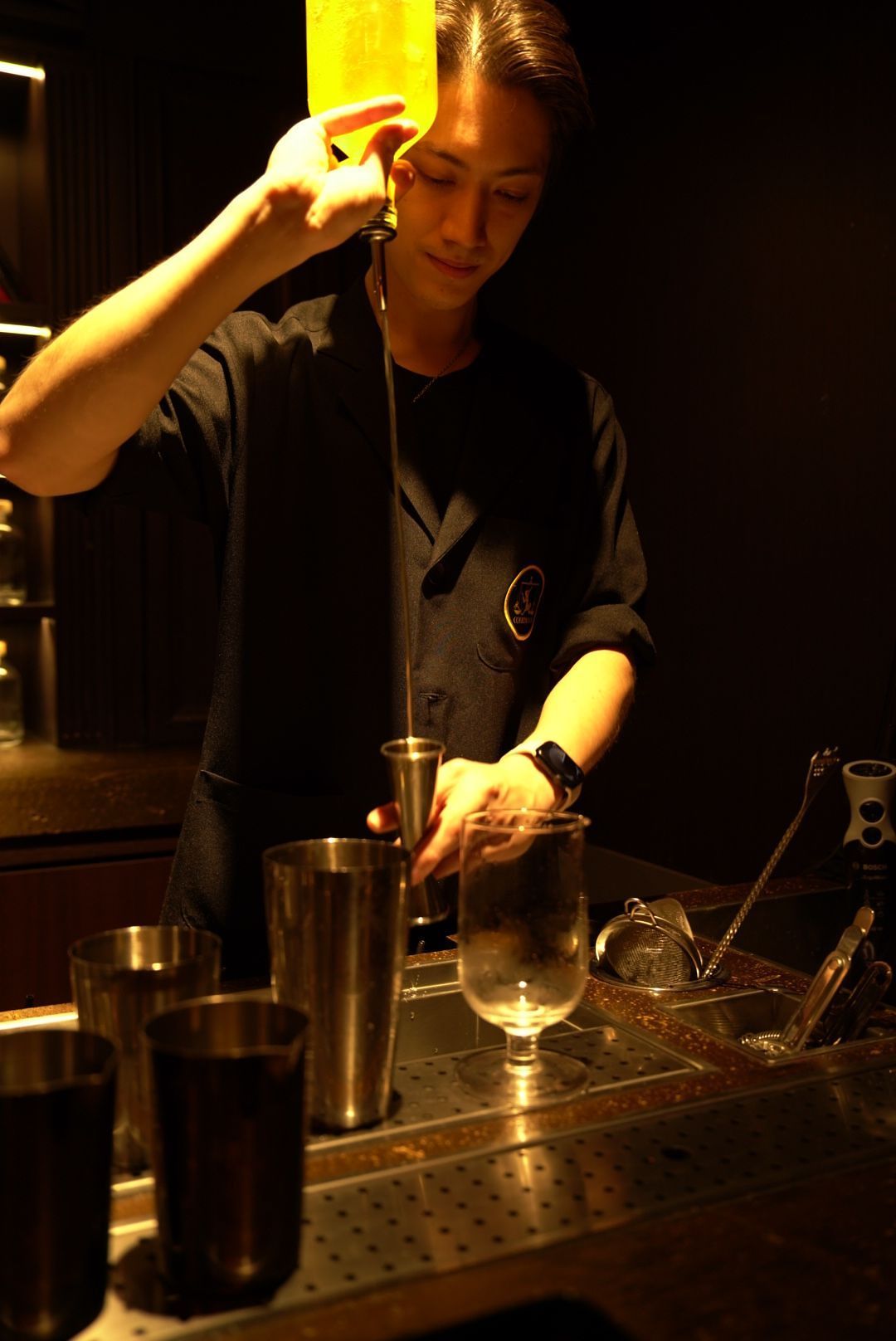 A bartender preparing drinks at a bar counter with cocktail equipment and shakers.