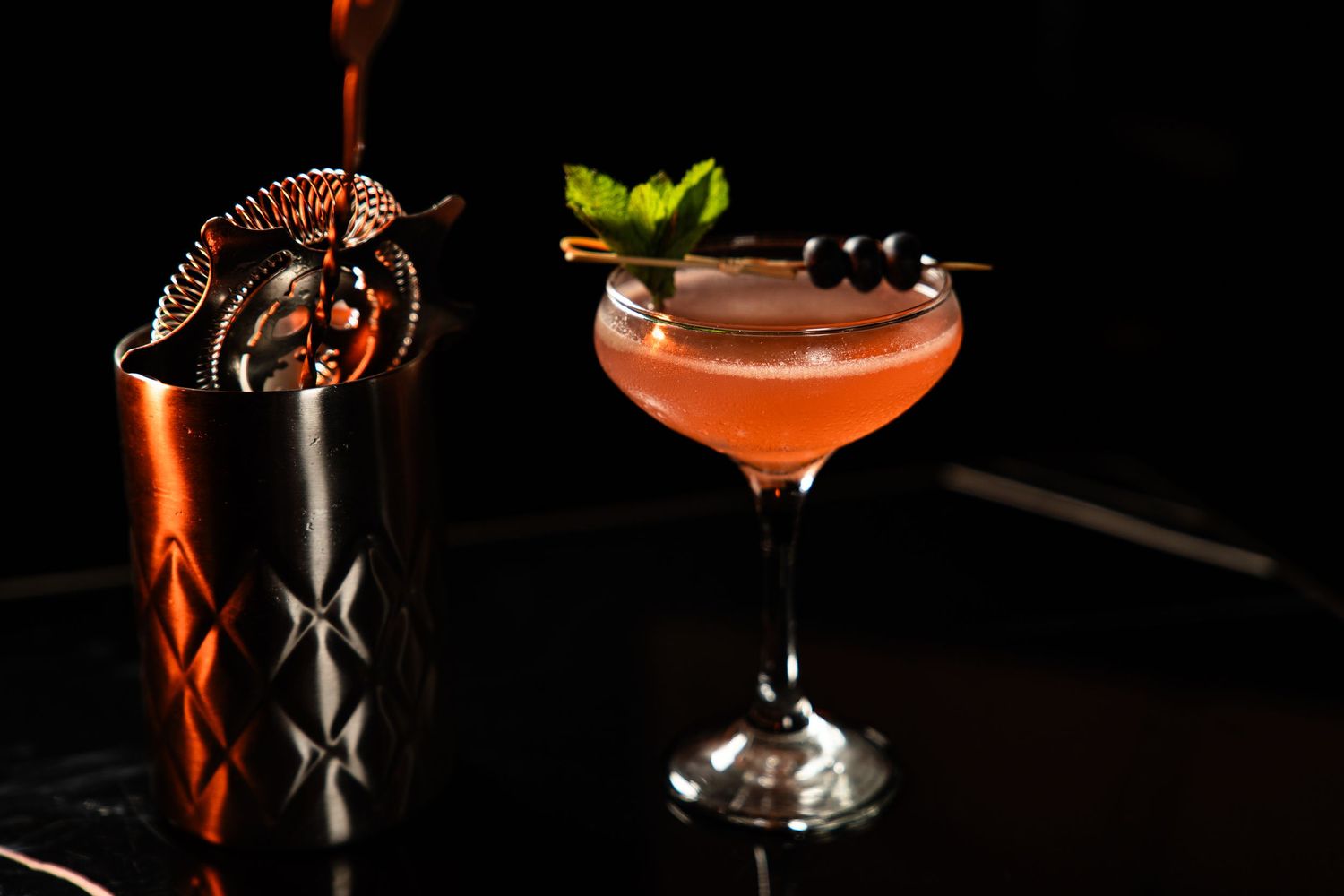 Two craft cocktails with elegant garnishes and metal shaker on dark wooden surface.