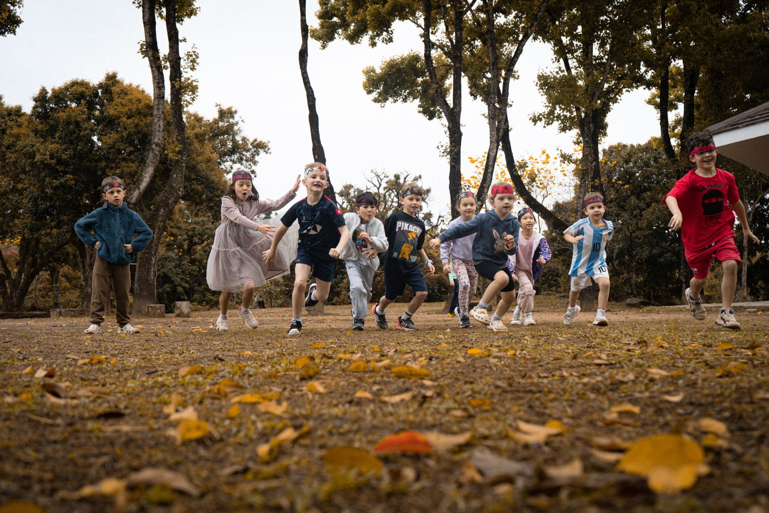 Group running together across leaf-covered ground during fall outdoor event.