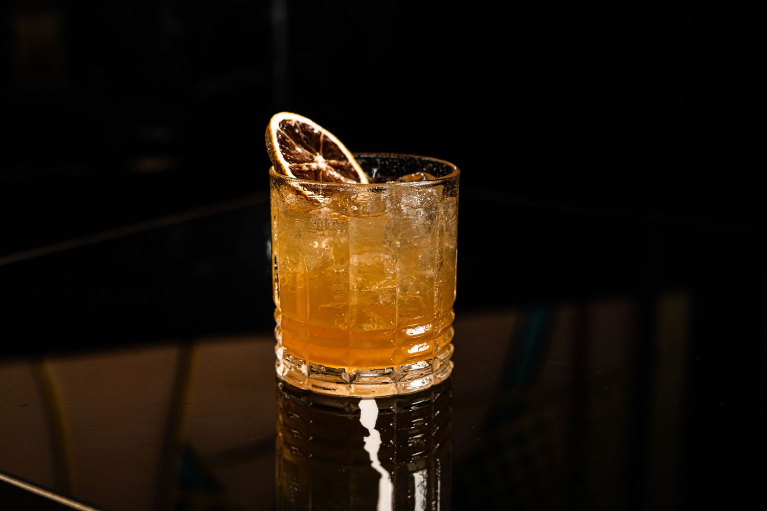 A bourbon cocktail served in a crystal rocks glass with ice and garnished with a dried citrus wheel.